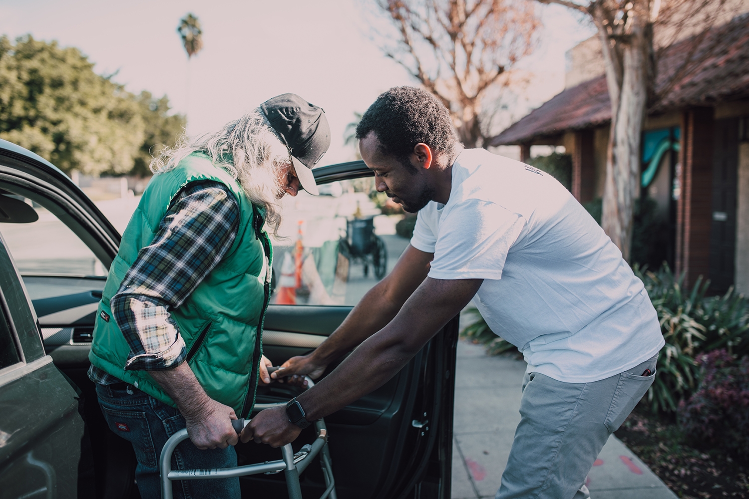 A man gives mutual aid by providing a ride to an older resident and helping him out of the car to use his mobility device.